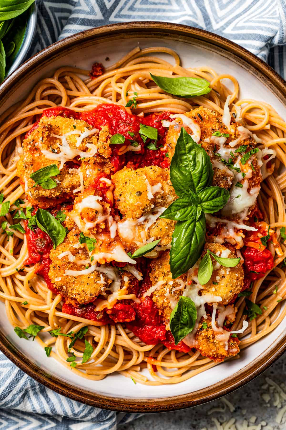 Breaded shrimp parmesan served over pasta in a bowl and garnished with fresh basil.