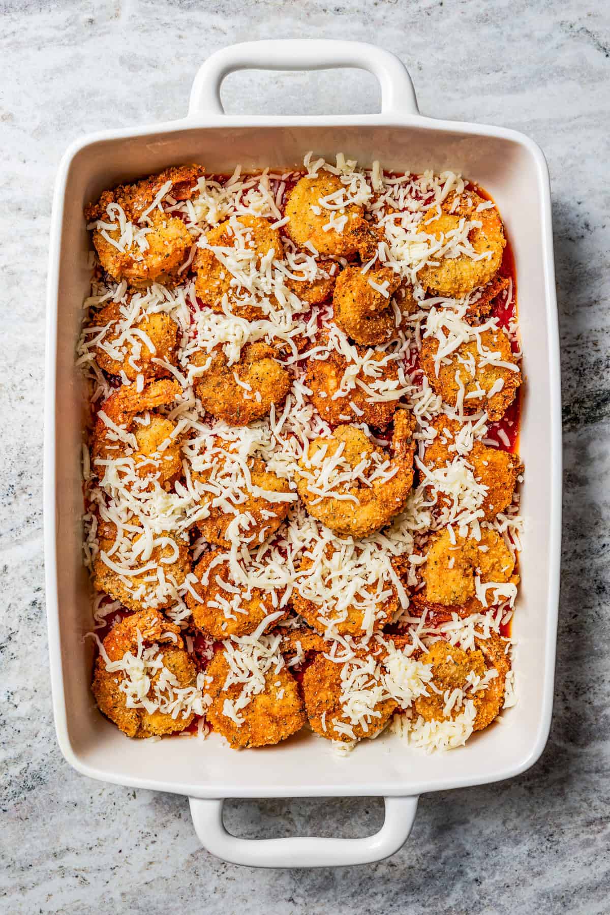 Shrimp layered over marinara and topped with grated cheese in a baking dish.