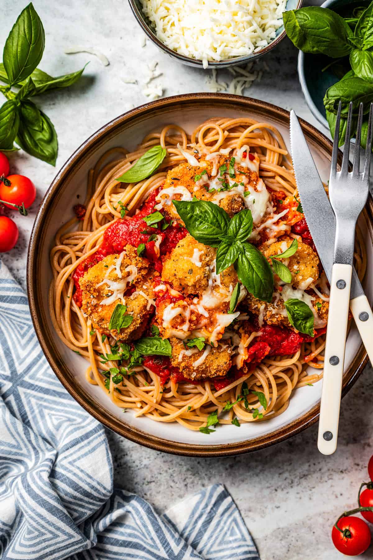 Shrimp parmigiana served over spaghetti in a bowl, with a knife and fork resting on the edge of the bowl.