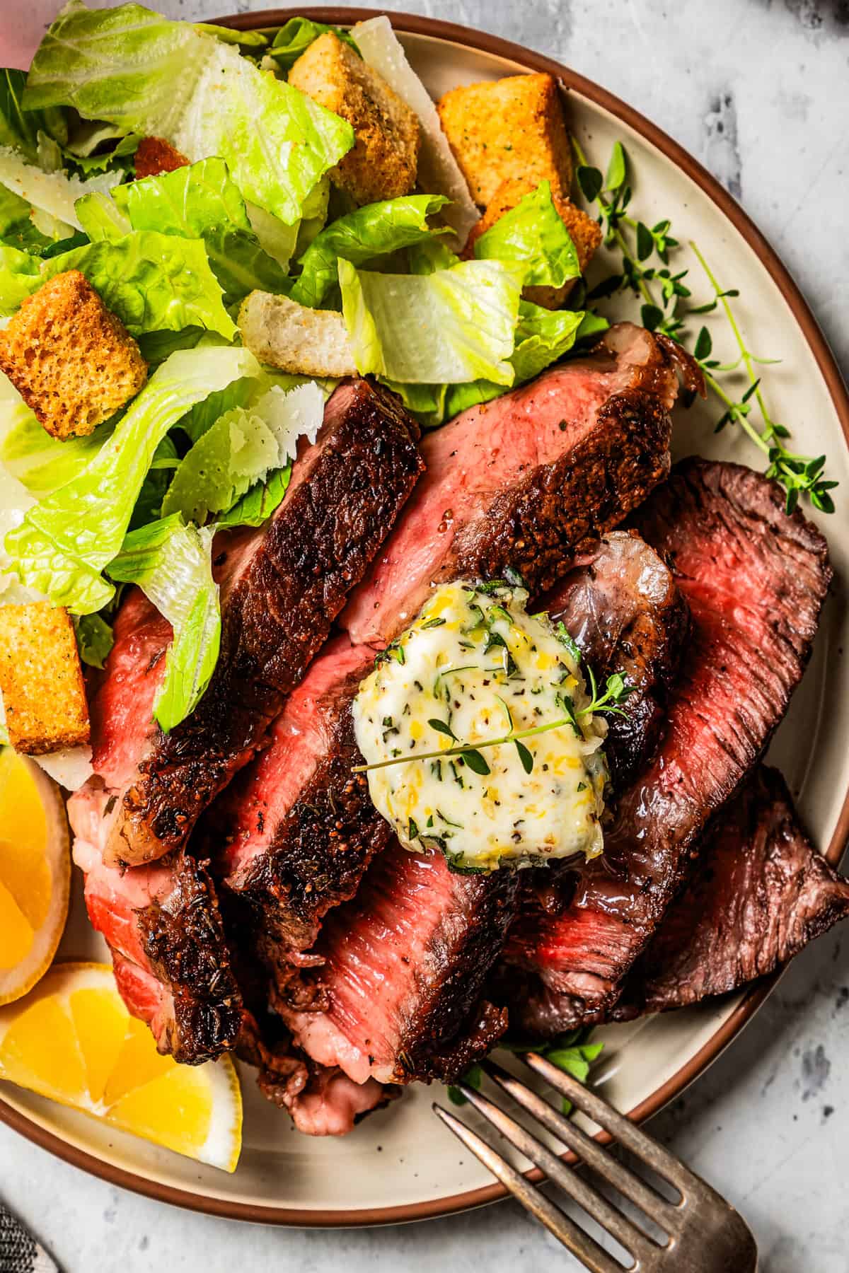 Slices of steak served with a green salad, with a pat of herbed butter set over the meat.