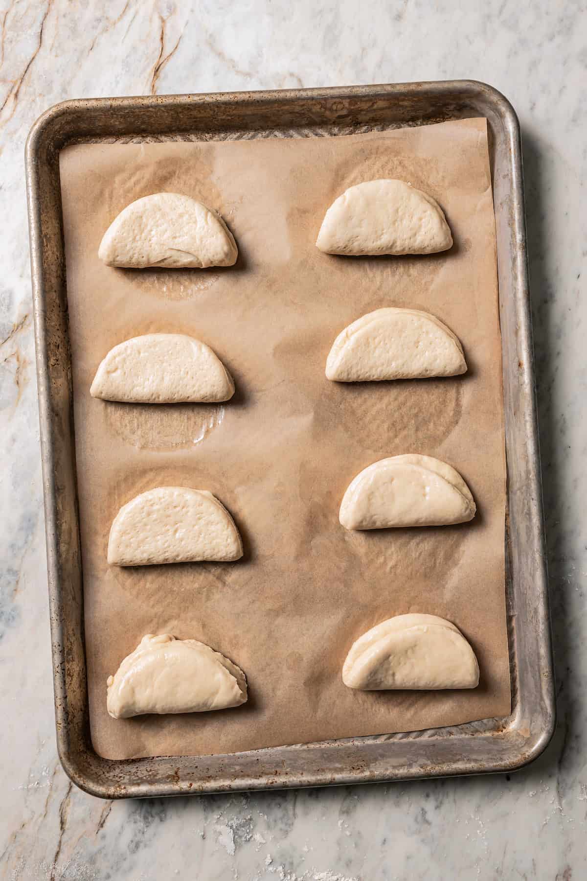 Shaped bao buns on a parchment-lined baking sheet.