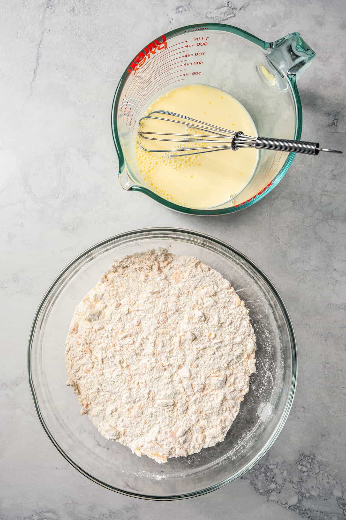 Wet ingredients combined in a spouted glass bowl with a whisk, next to a second glass bowl with dry ingredients.