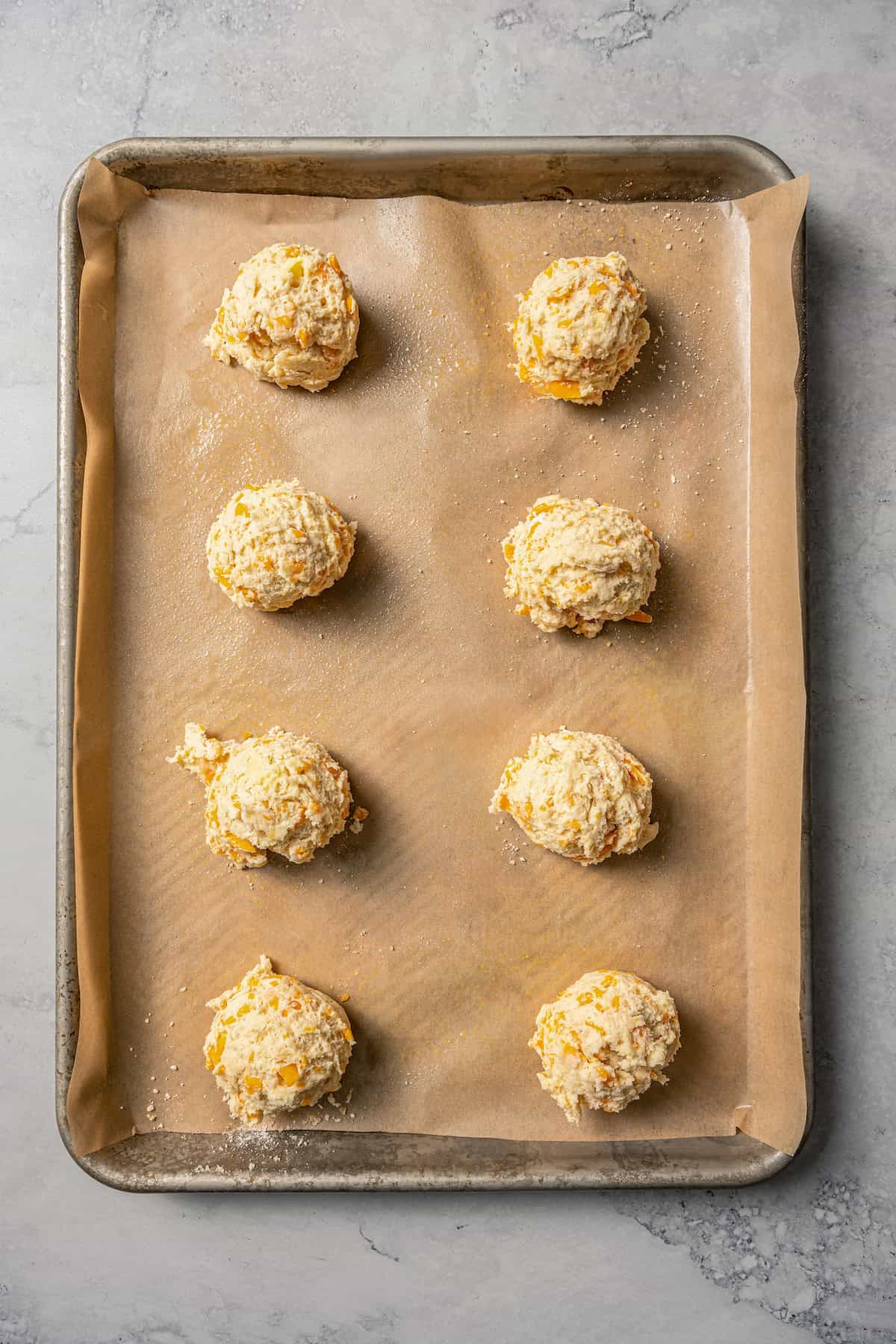 Cheddar bay biscuit dough balls dropped in rows on a lined baking sheet.