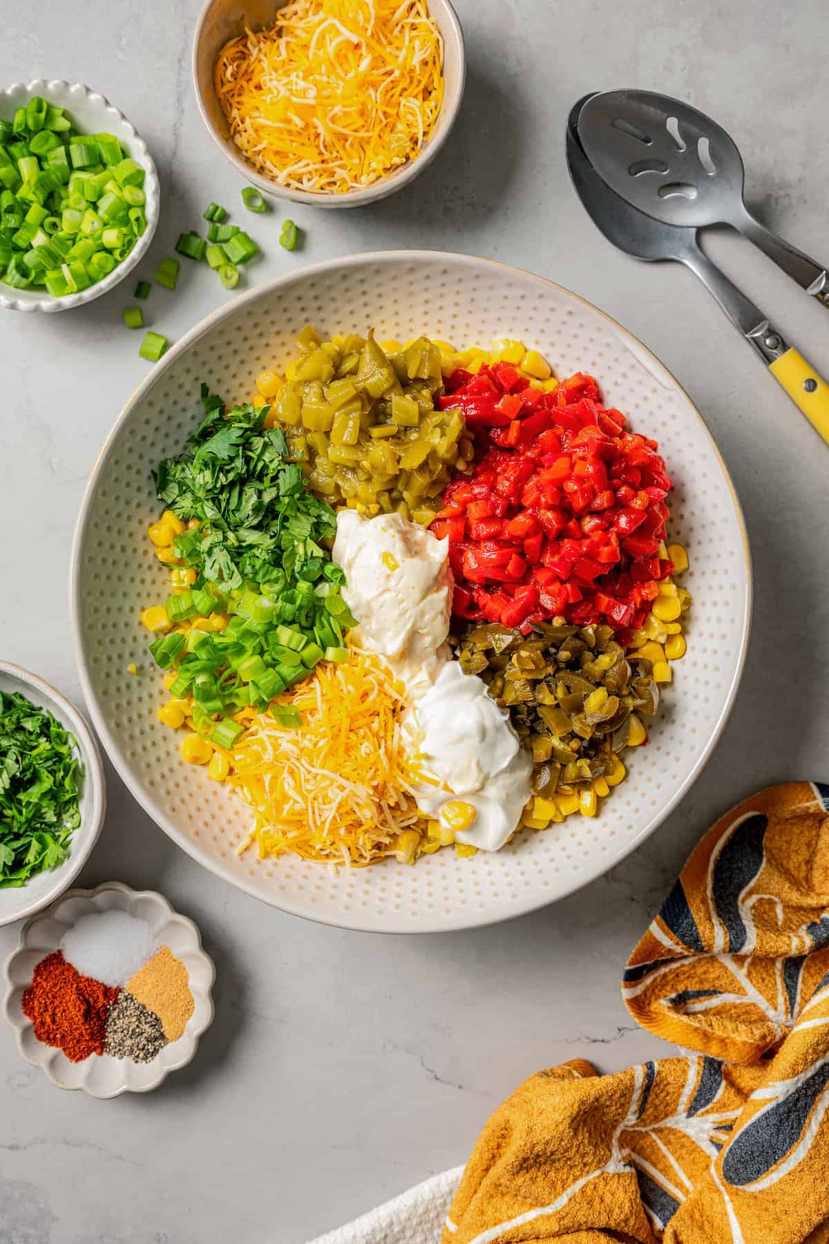 Corn dip ingredients combined in a serving bowl, surrounded by smaller bowls of ingredients.