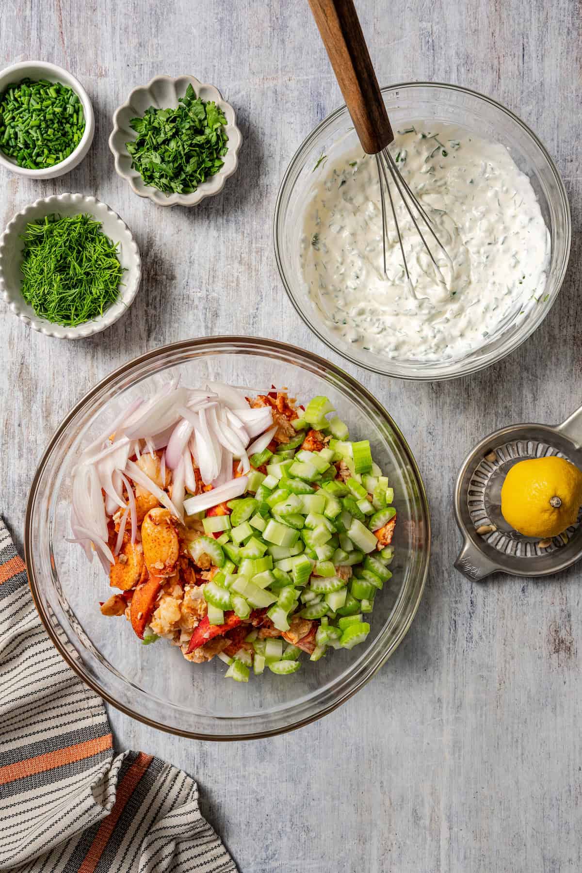 Overhead view of lobster roll ingredients combined in a glass bowl, next to a second bowl with dressing.