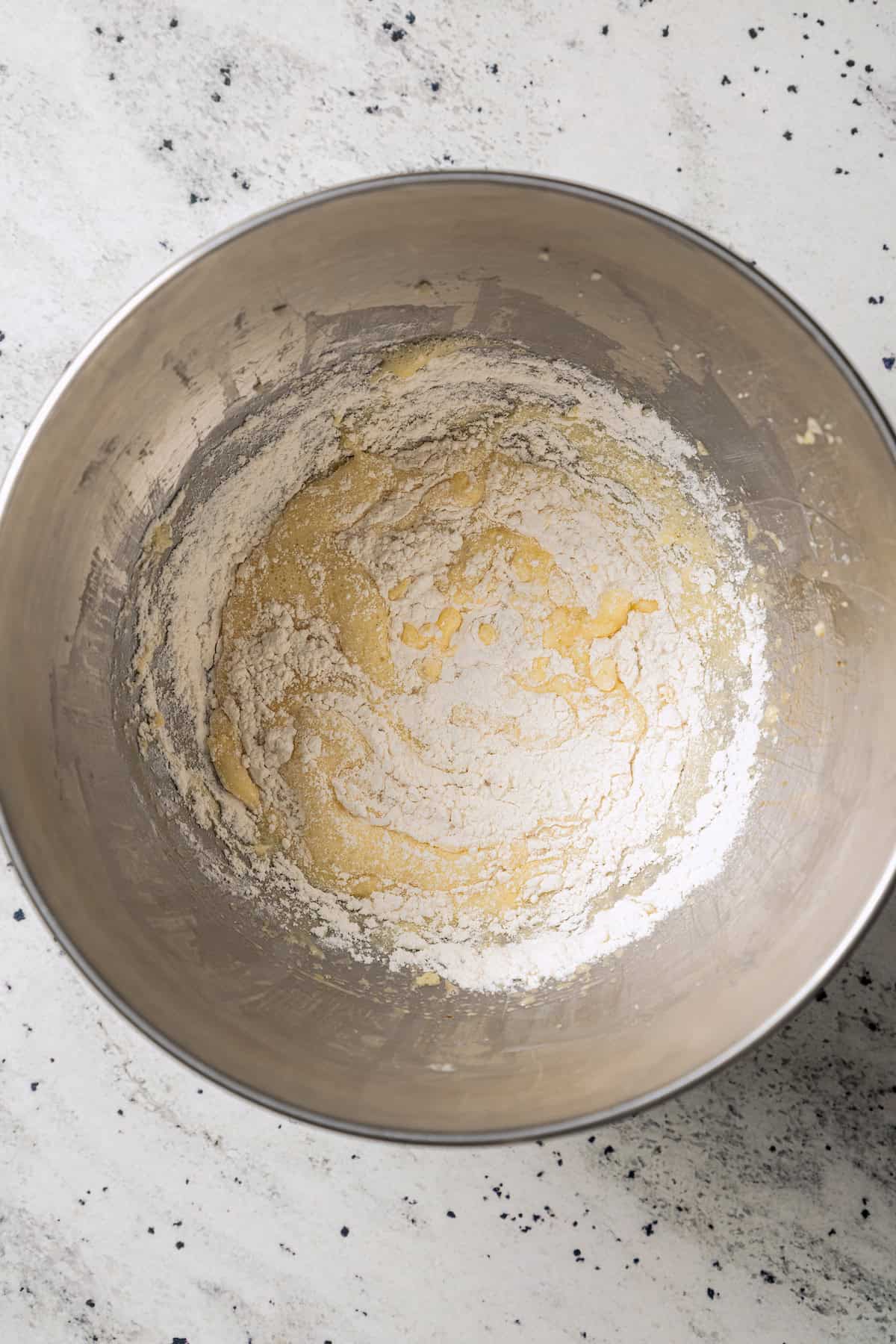 Dry ingredients added to wet cake batter in a metal mixing bowl.