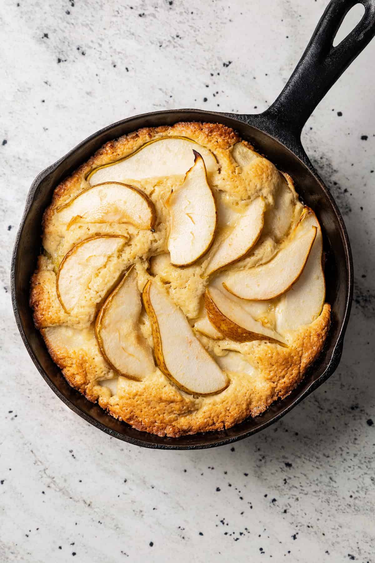 Baked pear cake garnished with pear slices in a skillet.