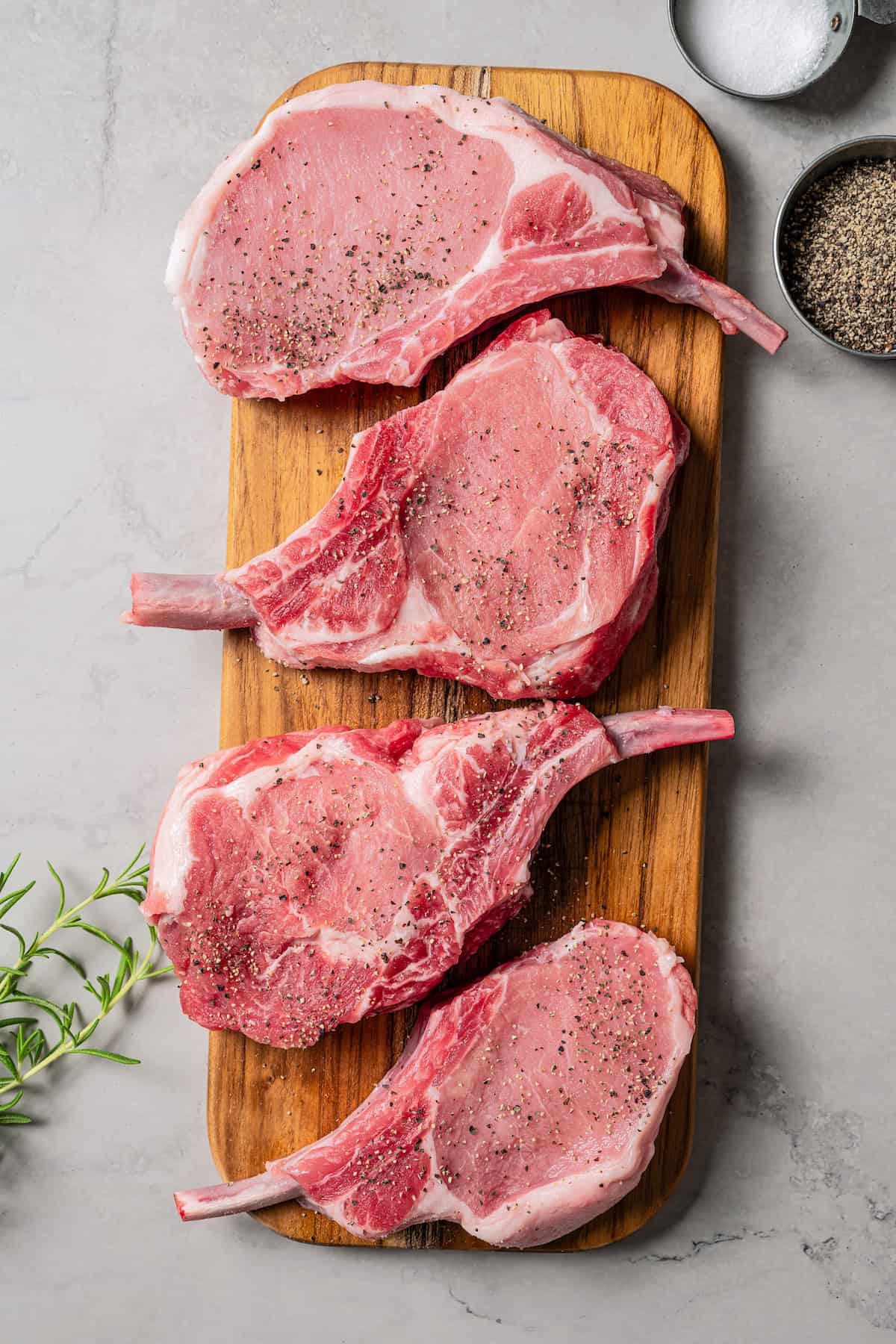 Four uncooked seasoned tomahawk pork chops on a wooden cutting board.