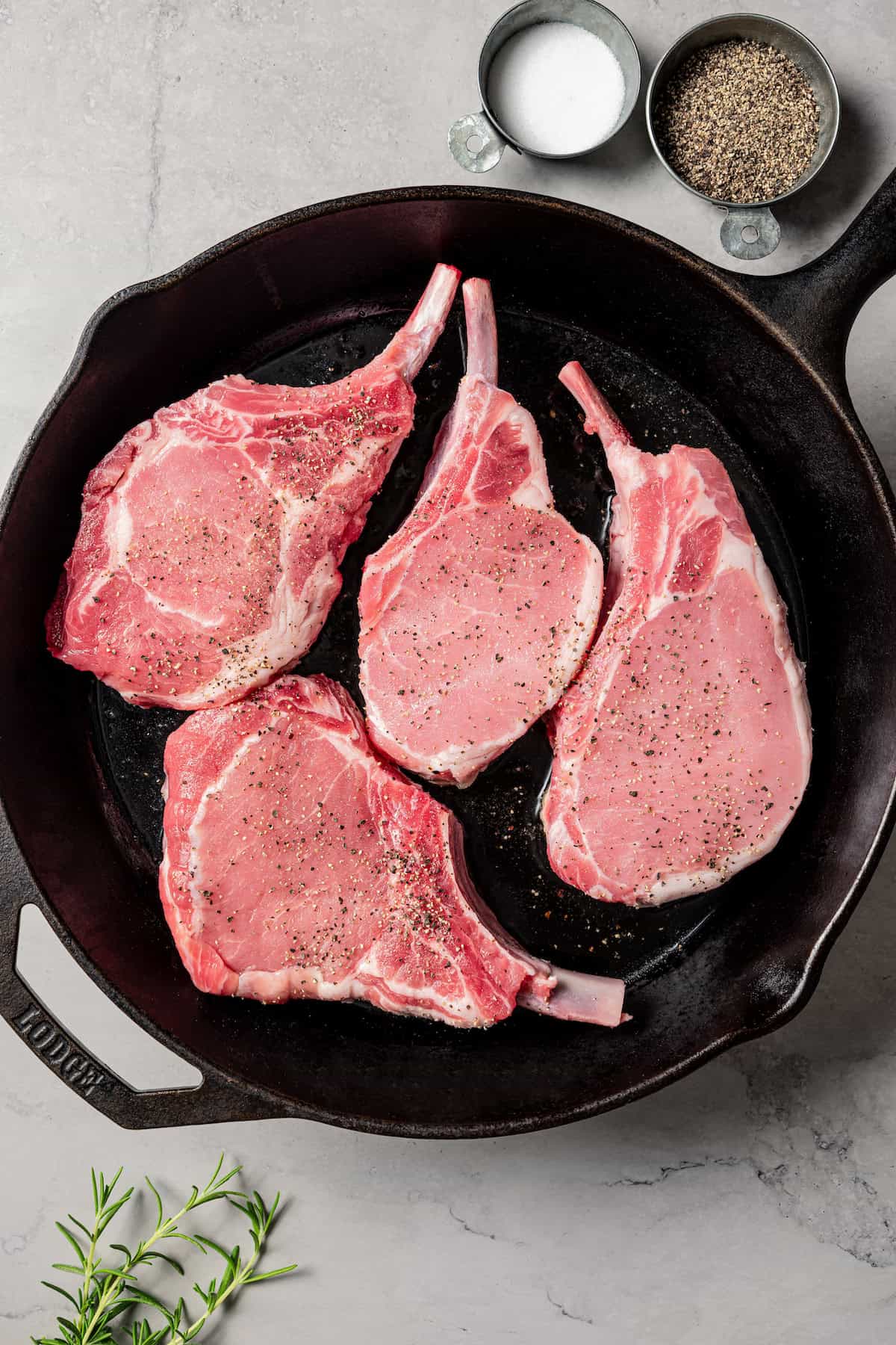 Four uncooked tomahawk pork chops in a skillet.