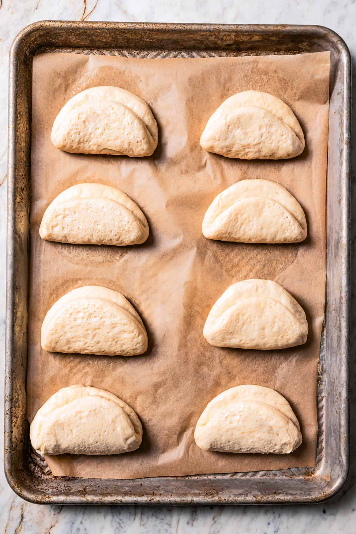 Shaped bao buns after rising on a parchment-lined baking sheet.