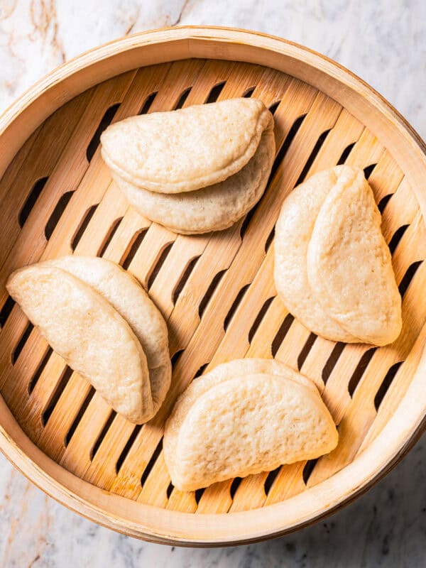 Four steamed bao buns in a bamboo steamer basket.