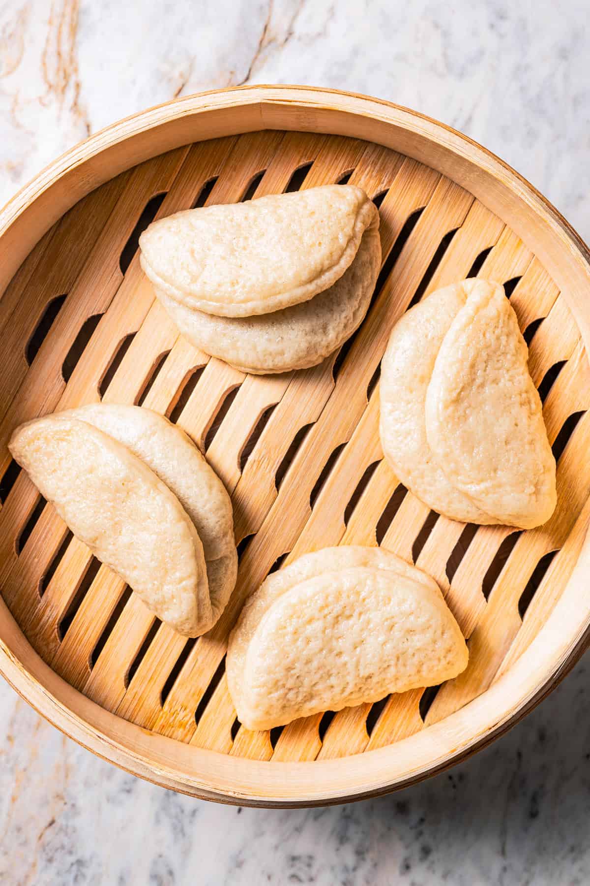 Four steamed bao buns in a bamboo steamer basket.