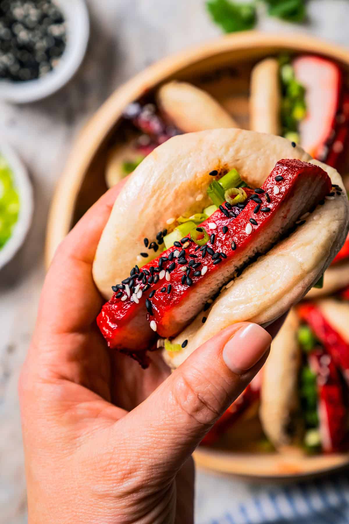 Close up of a hand holding a char siu bao with more bao buns in a dumpling steamer in the background.