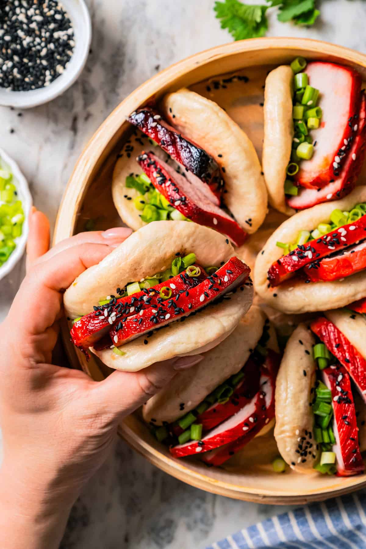 Overhead view of a hand holding a char siu bao over more bao buns in a dumpling steamer.