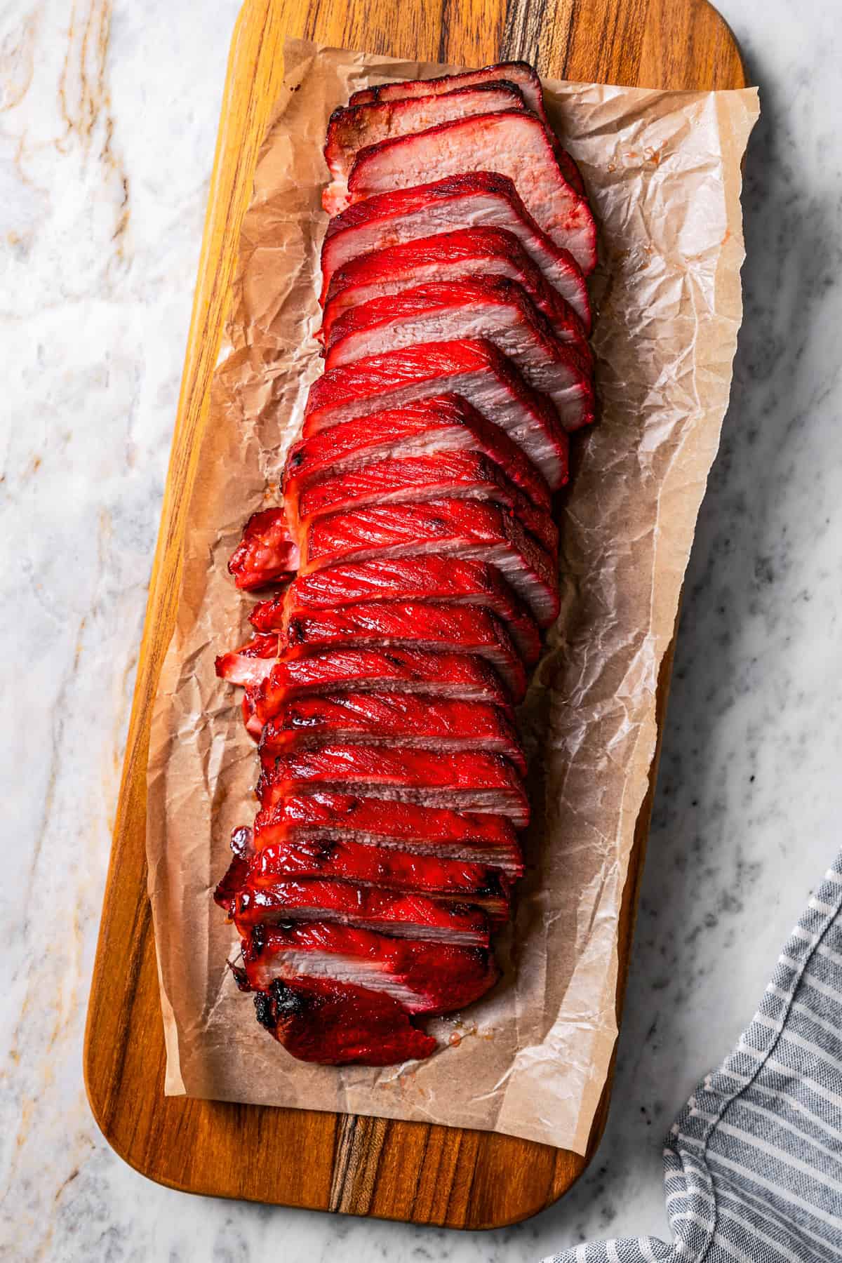 Char siu pork tenderloin cut into slices and arranged on a parchment-lined wooden cutting board.