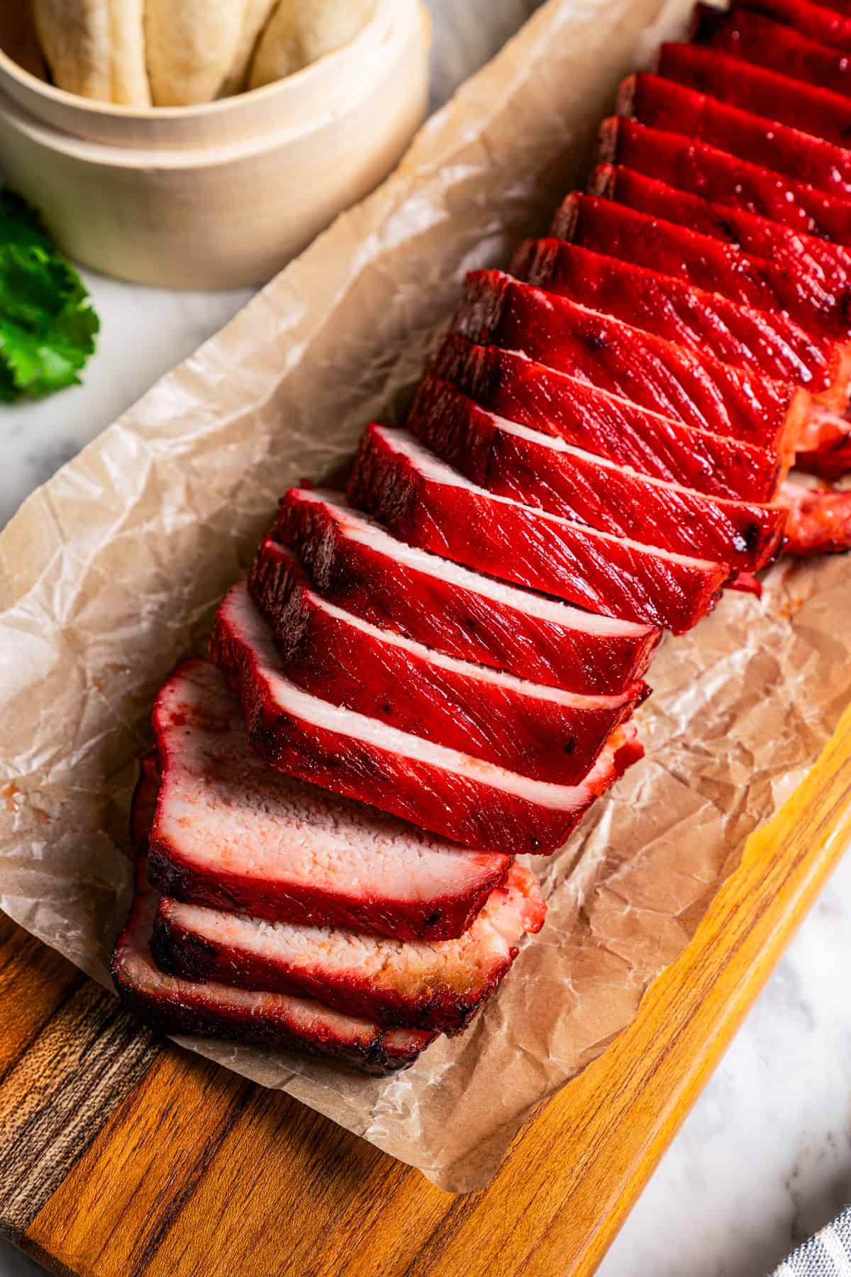 Char siu pork is cut into slices on a wooden cutting board.