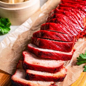 Char siu pork tenderloin cut into slices on a wooden cutting board.