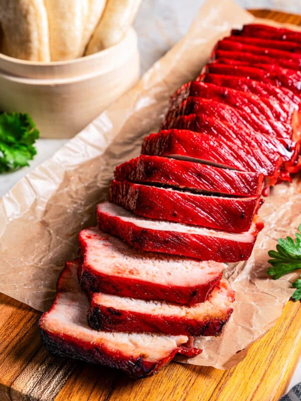 Char siu pork tenderloin cut into slices on a wooden cutting board.