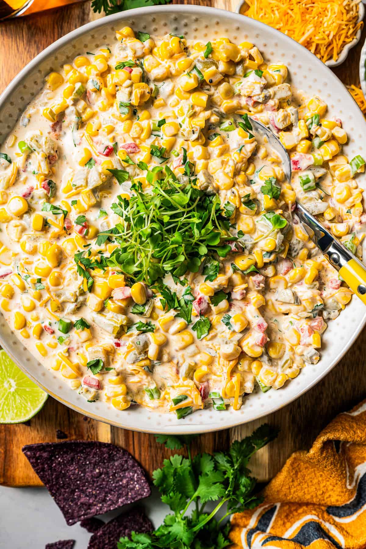 Overhead image of corn dip served in a bowl and garnished with chopped herbs in a bowl with a spoon.