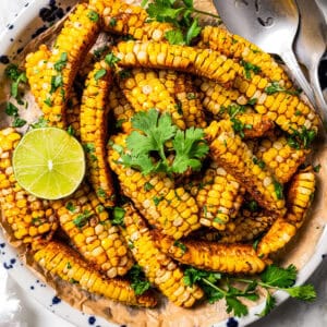 Corn ribs on a plate garnished with fresh cilantro and lime, with a serving spoon.