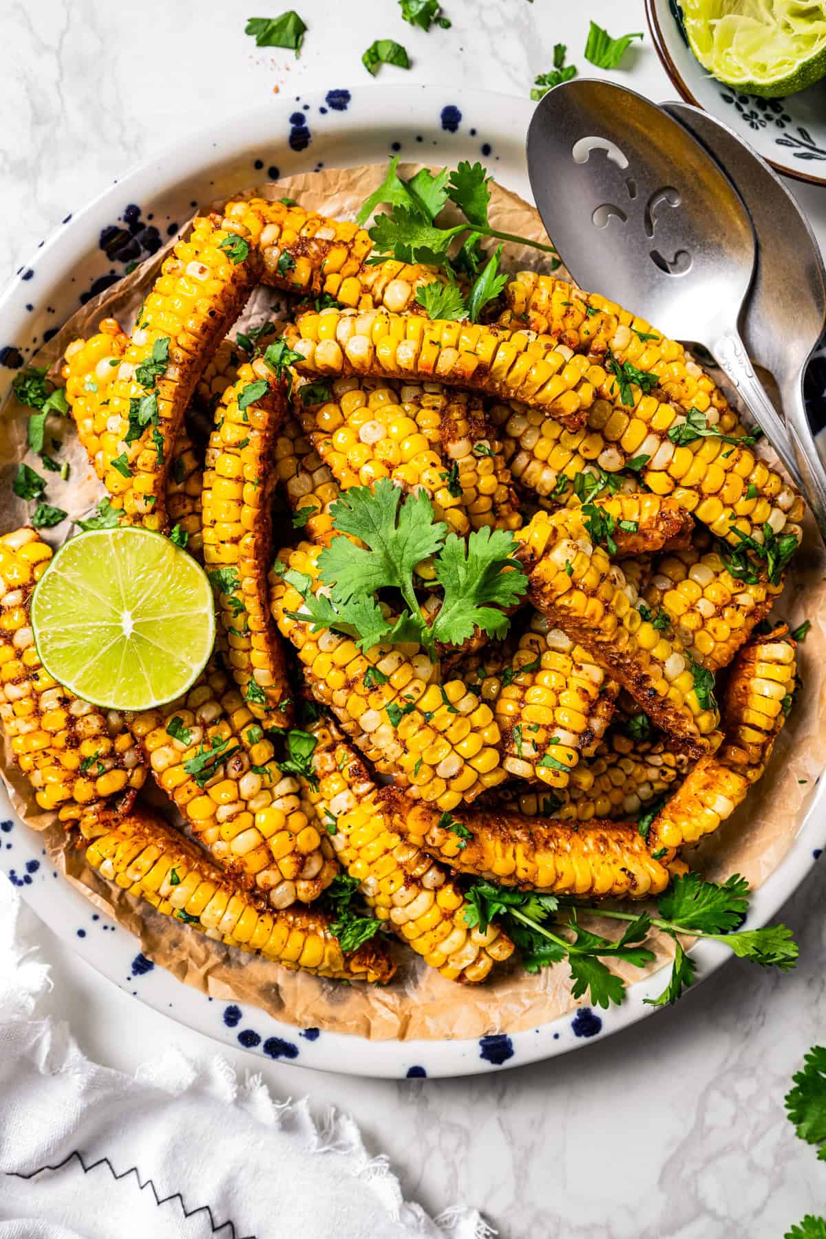 Corn ribs on a plate garnished with fresh cilantro and lime, with a serving spoon.