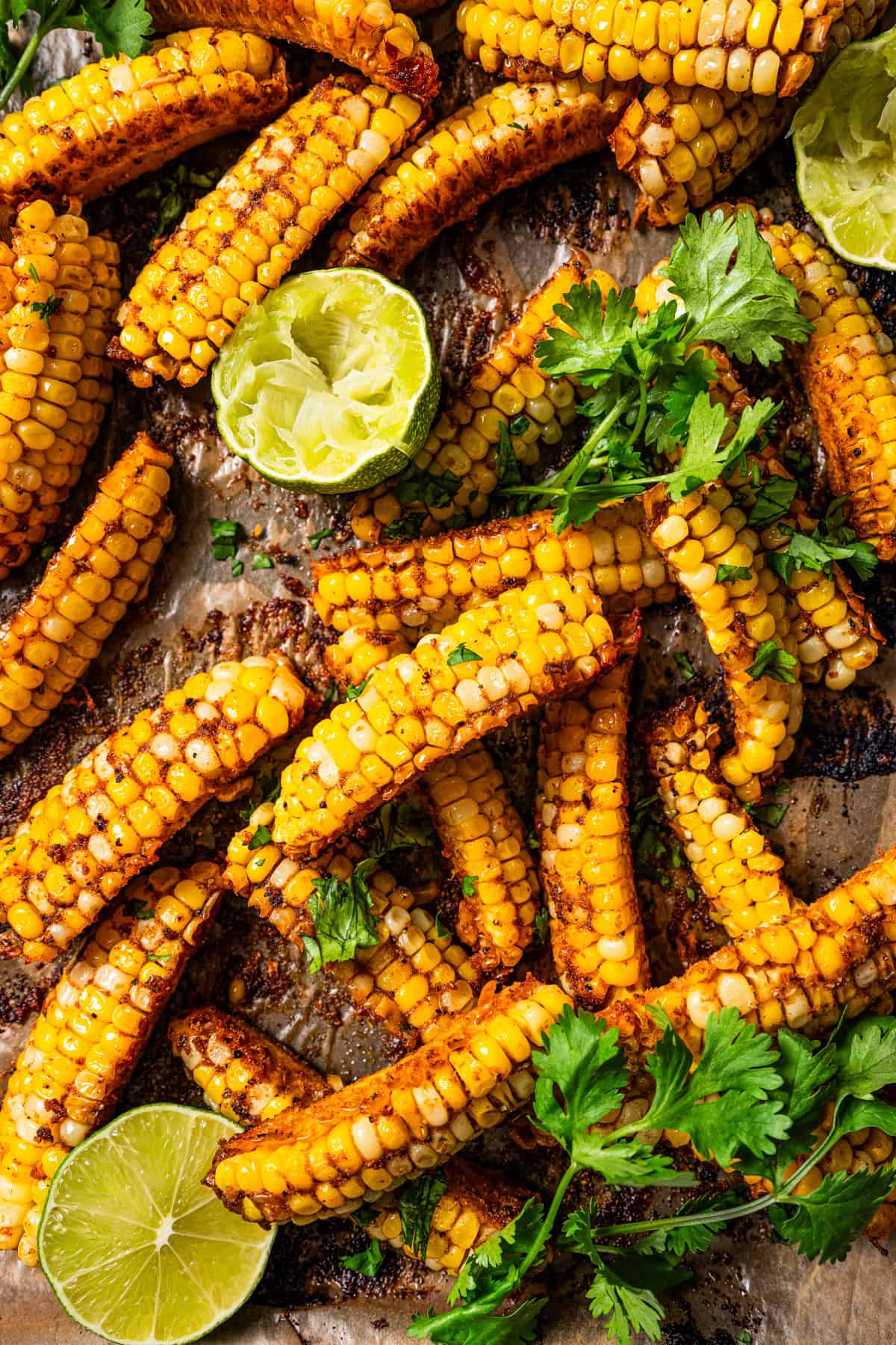 Ribs of cooked corn ribs with halved limes and fresh cilantro set on a brown parchment paper.