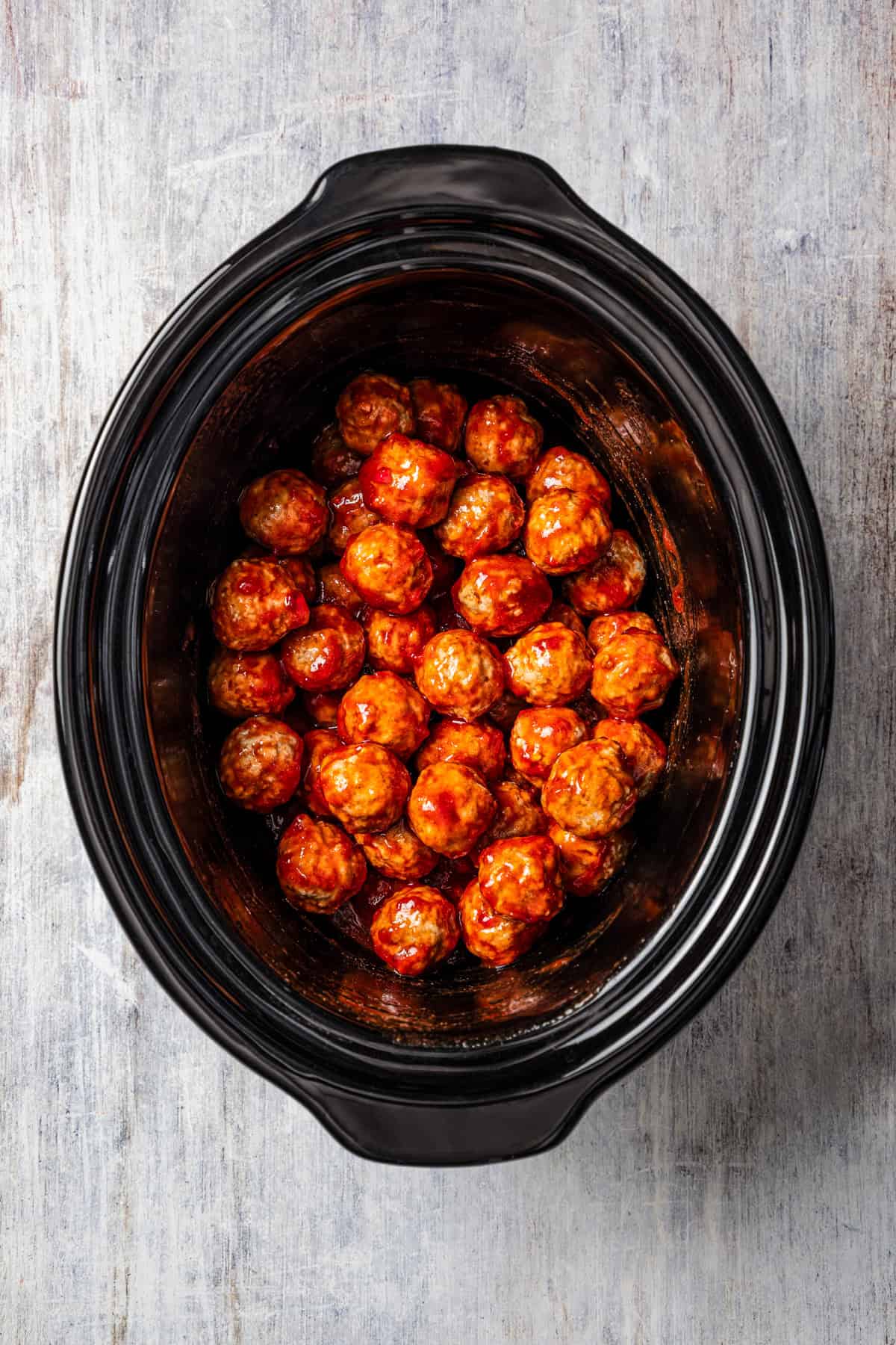 Meatballs added to a crock pot with grape jelly sauce.