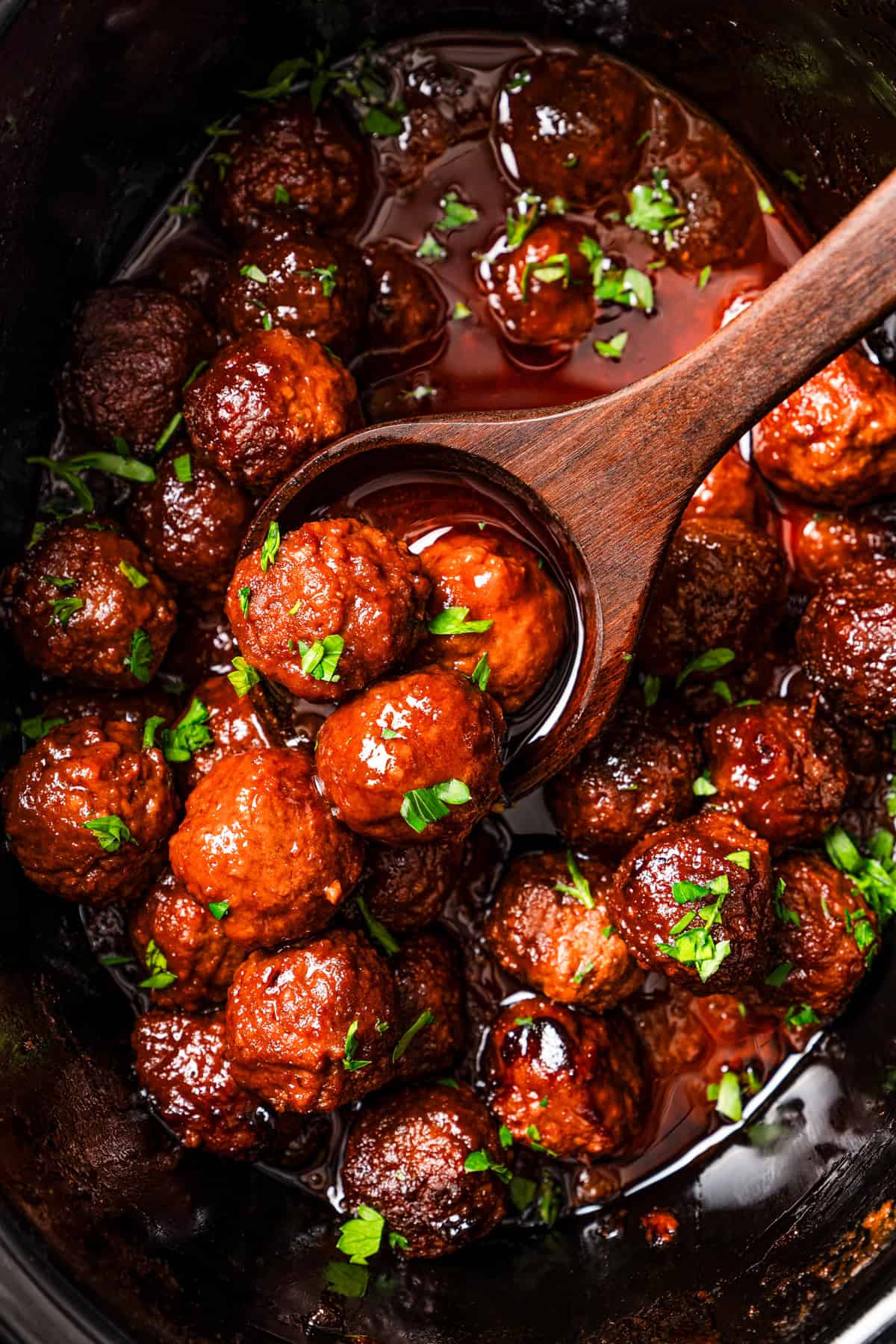 Grape jelly meatballs inside the crock pot with a wooden spoon.