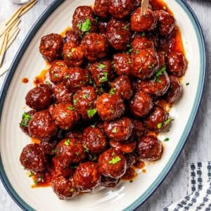 Overhead view of a platter of grape jelly meatballs next to a small glass of cocktail toothpicks.