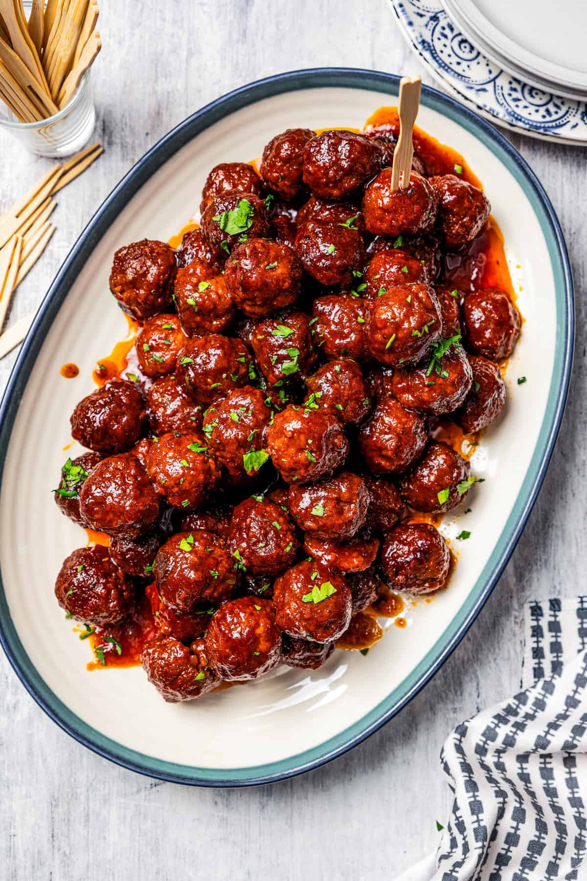 Overhead view of a platter of grape jelly meatballs next to a small glass of cocktail toothpicks.