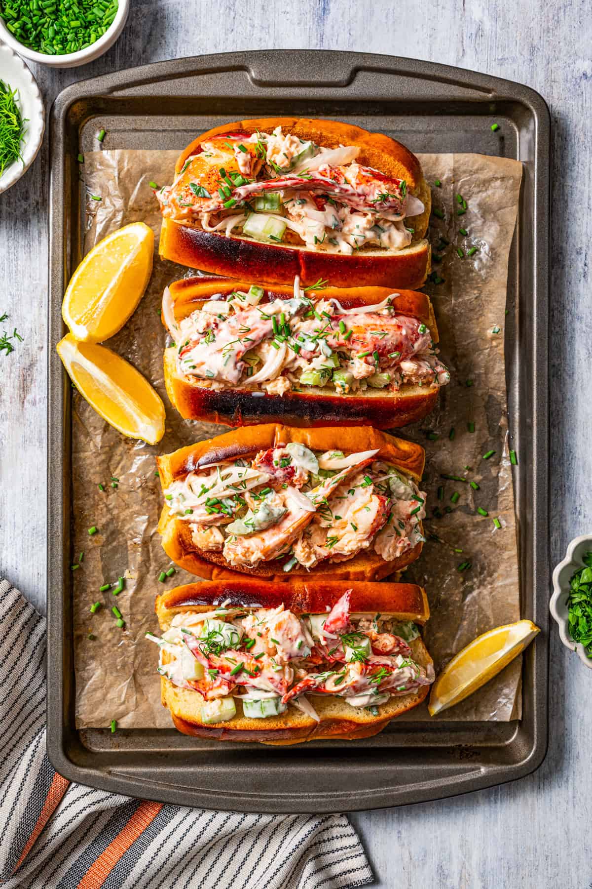 Four lobster rolls on a piece of parchment paper next to lemon wedges.