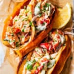 Overhead view of two homemade lobster rolls in a paper-lined food serving basket with a lemon wedge for garnish.