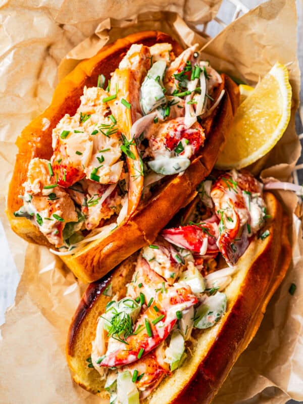 Overhead view of two homemade lobster rolls in a paper-lined food serving basket with a lemon wedge for garnish.