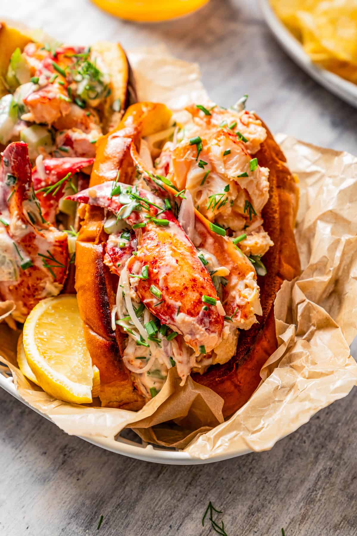 Two homemade lobster rolls in a paper-lined food serving basket.