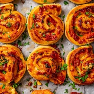 Overhead view of rows of pepperoni pizza rolls on parchment-lined baking sheet.