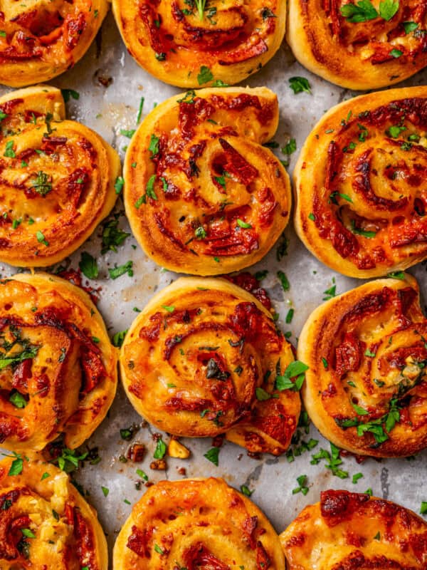 Overhead view of rows of pepperoni pizza rolls on parchment-lined baking sheet.