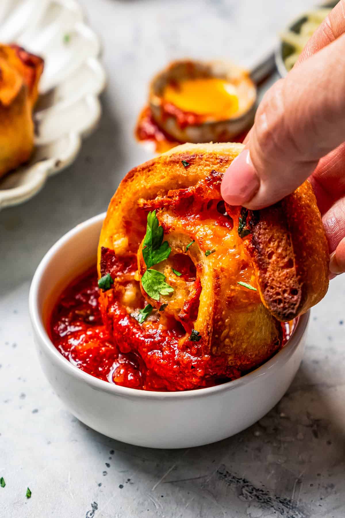 A hand dipping a pizza roll into a small bowl of marinara sauce.