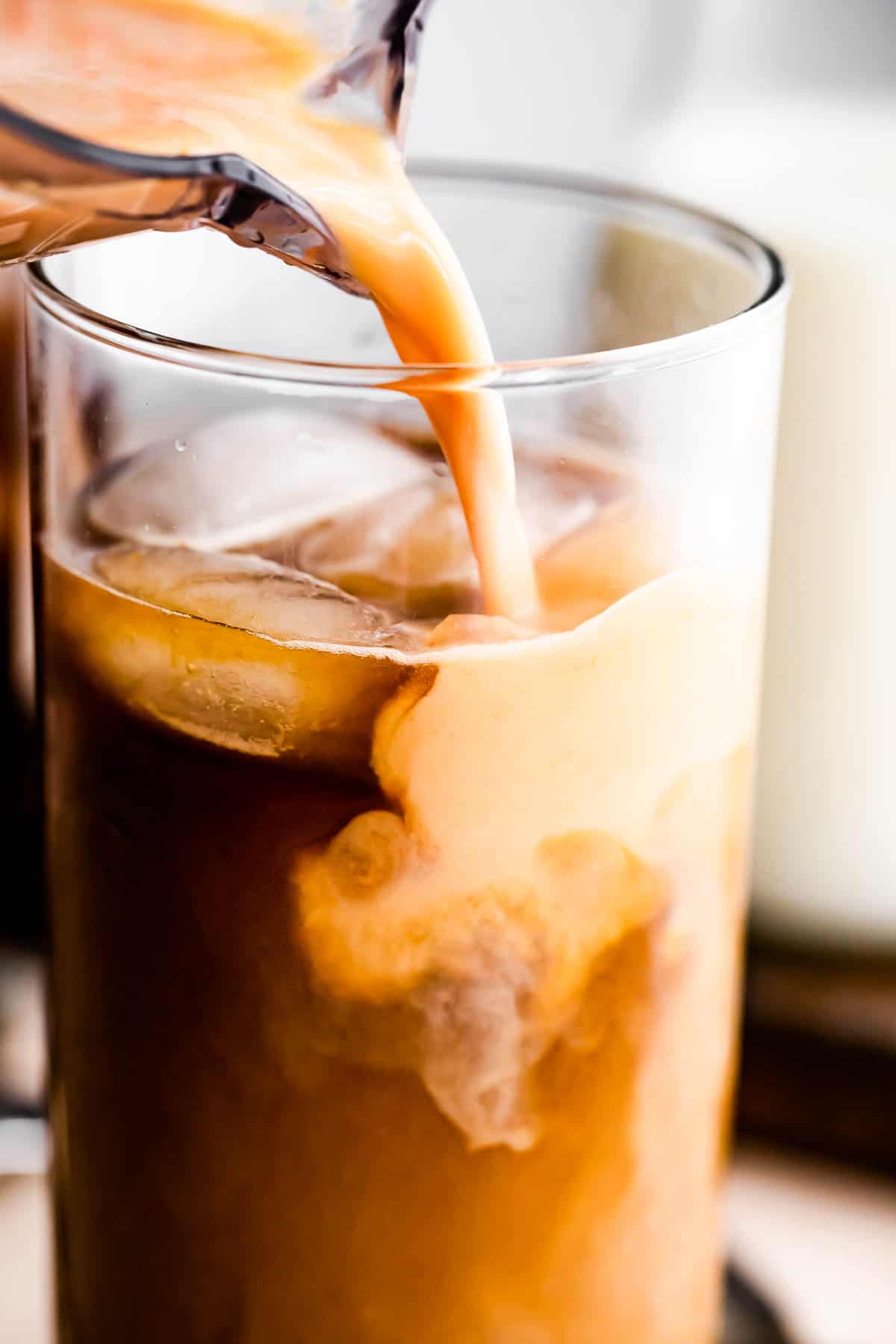 Pouring homemade pumpkin creamer into a tall glass of iced coffee.