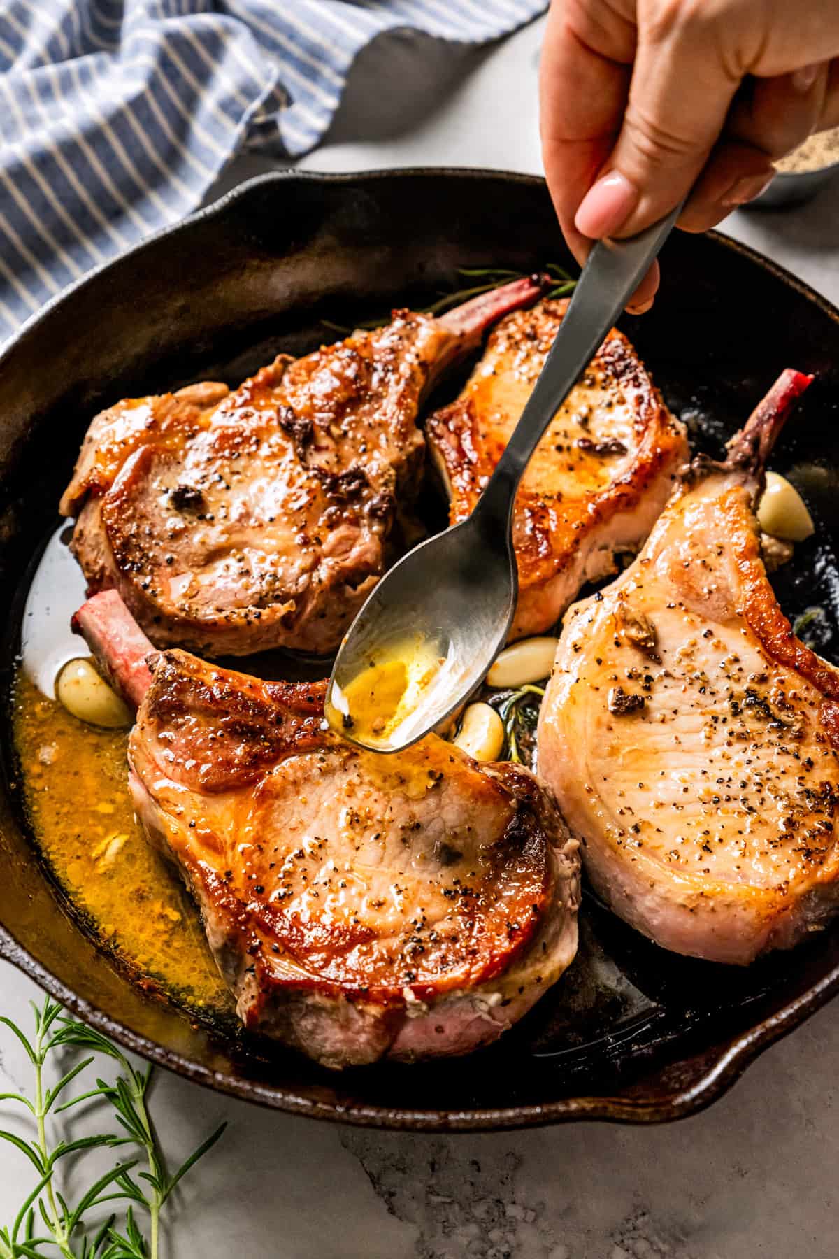 A hand using a spoon to baste tomahawk pork chops in a skillet.