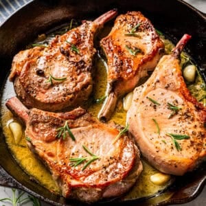 Four seared tomahawk pork chops in a skillet.