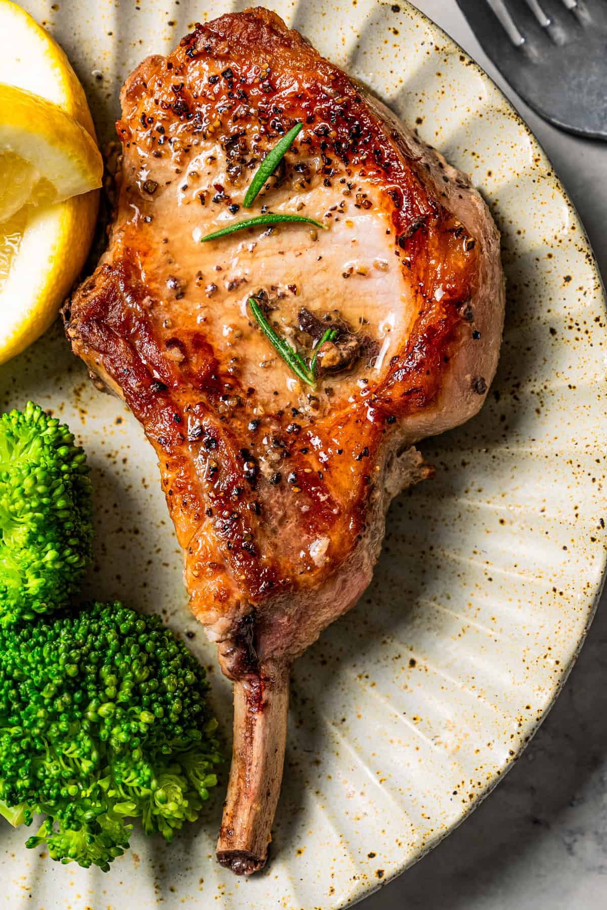 Bone in pork chop served on a dinner plate with a side of broccoli.