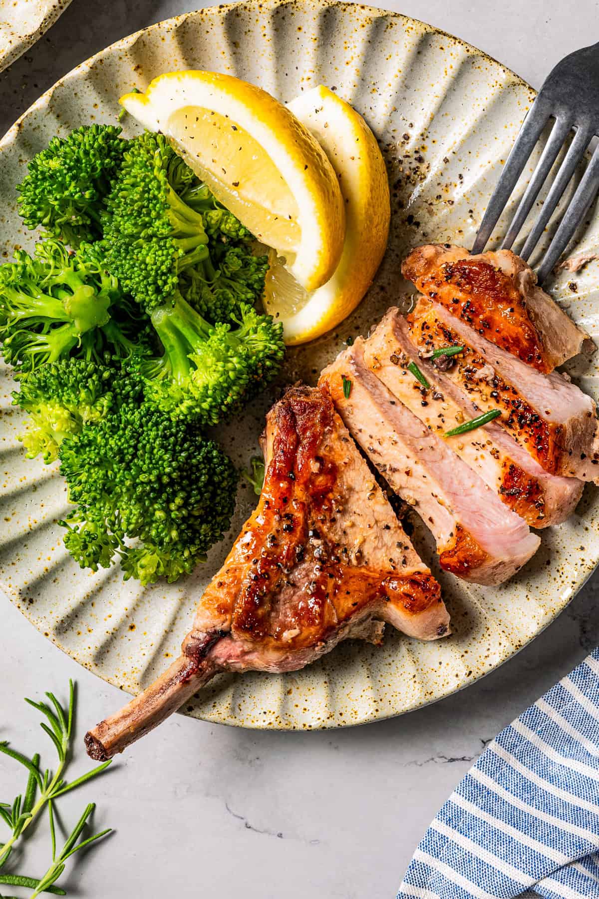 Sliced bone in pork chops on a plate with broccoli and lemon slices.