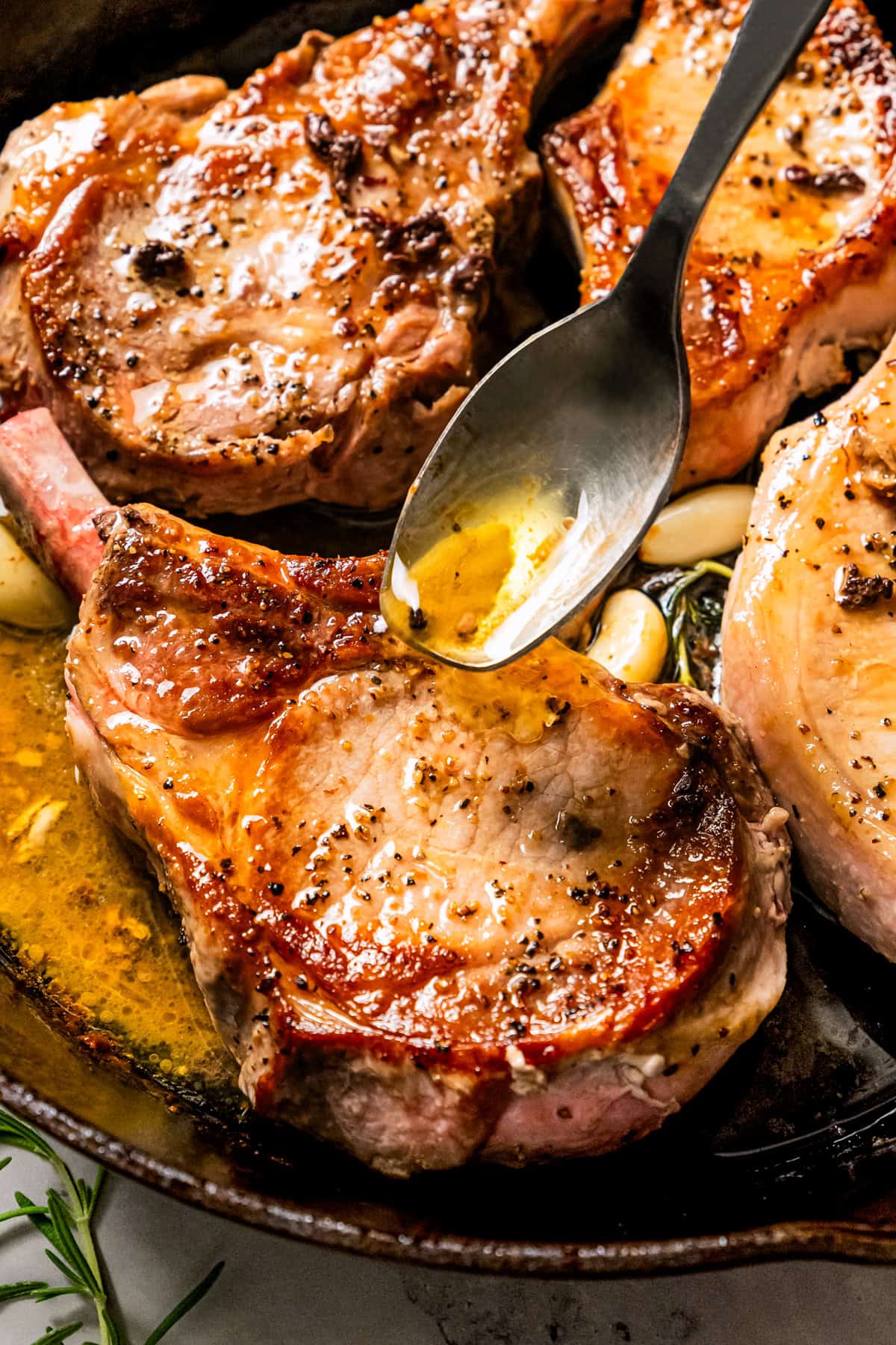 A hand using a spoon to baste tomahawk pork chops in a skillet.