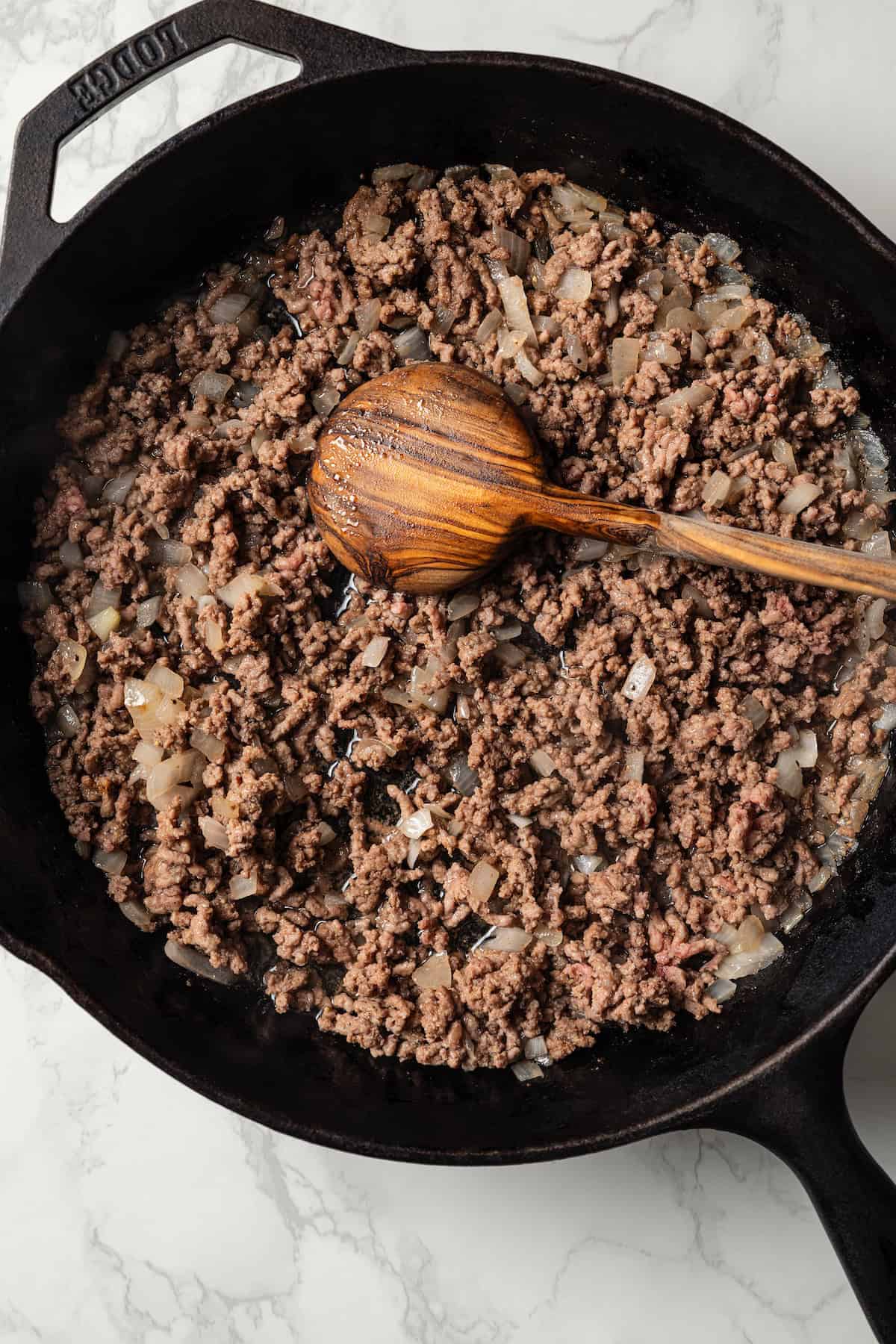 Browned ground beef in a skillet with a wooden spoon.