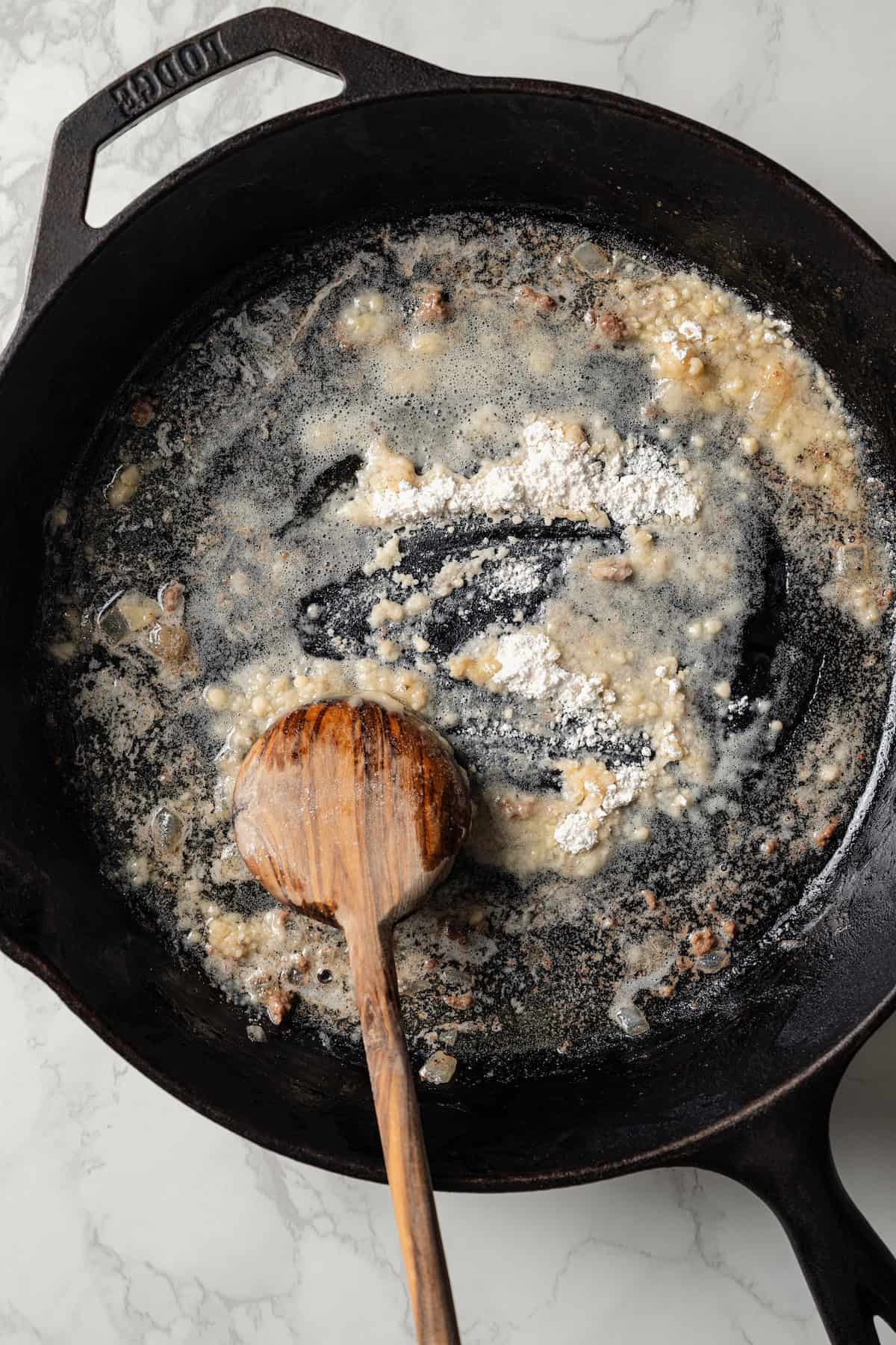 Flour being stirred into a skillet of melted butter with a wooden spoon, to make a roux.