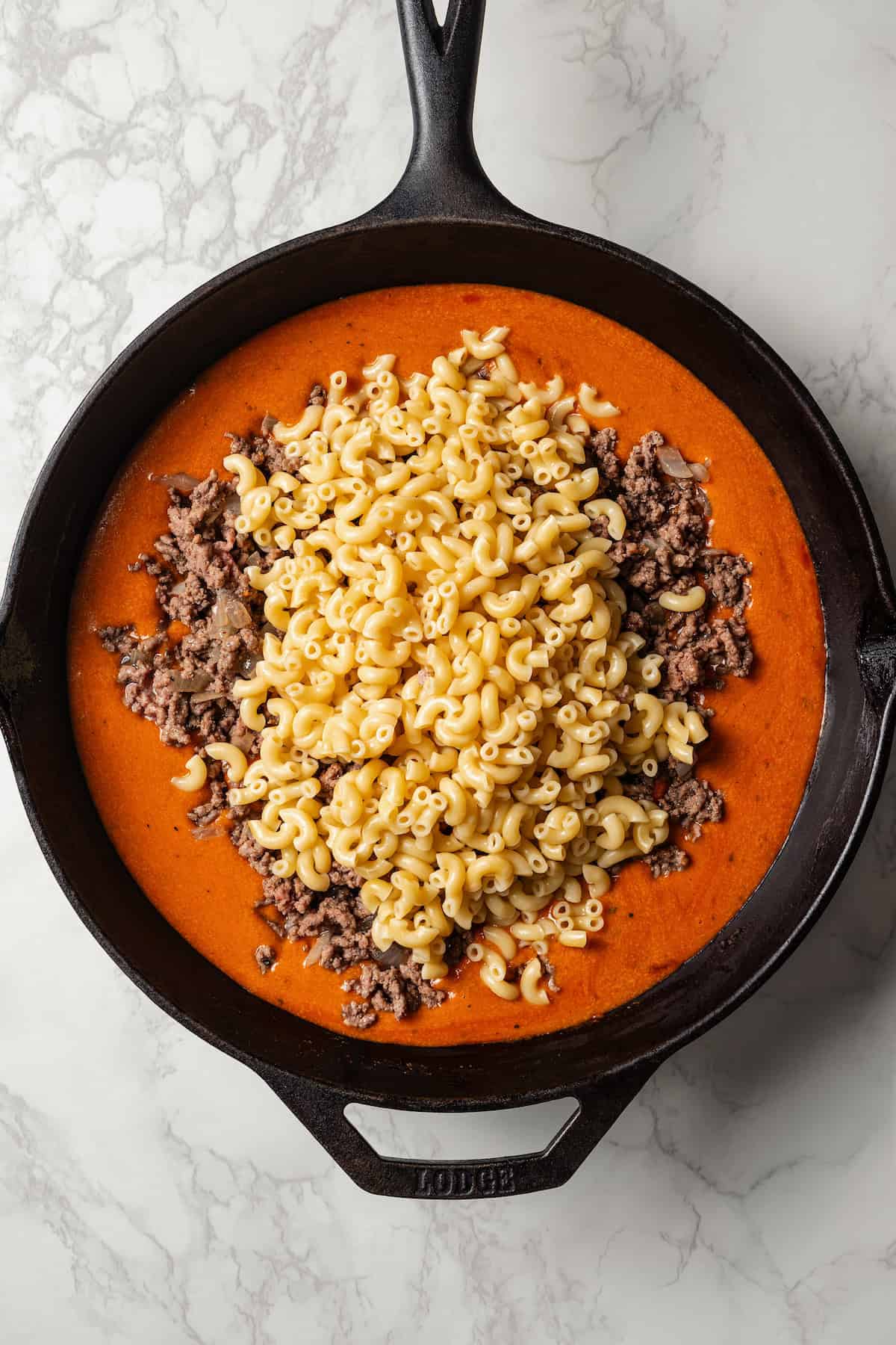 Noodles and cooked ground beef added to tomato sauce in a large skillet.