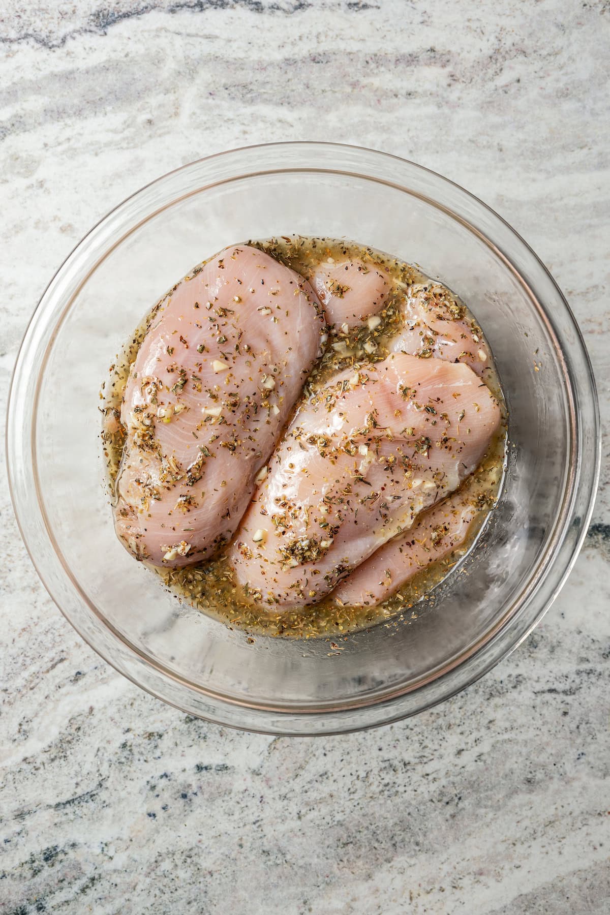 Chicken breasts marinating in a bowl with seasonings.