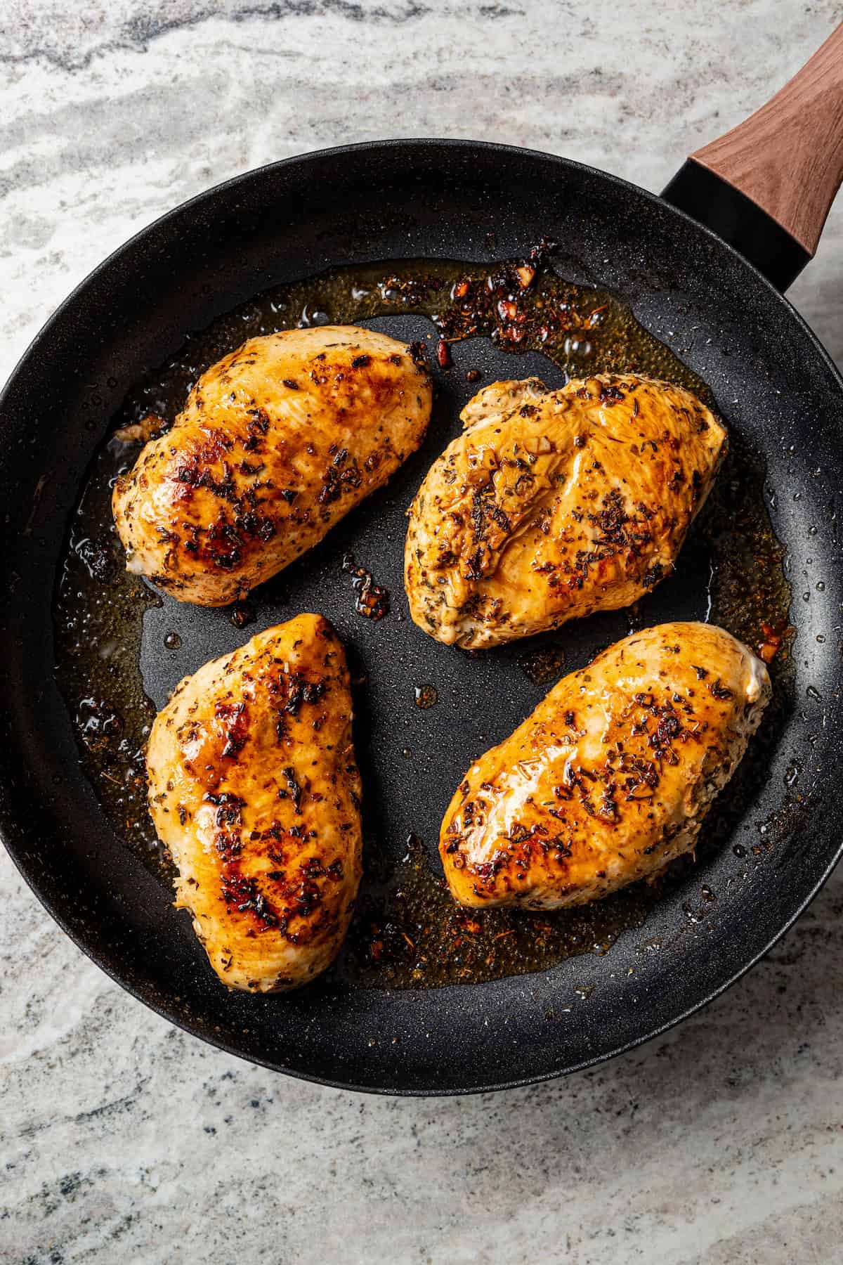 Four seared chicken breasts in a skillet.