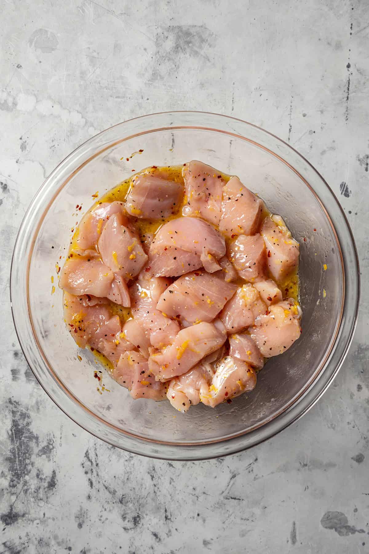 Chicken pieces marinating in a glass bowl.