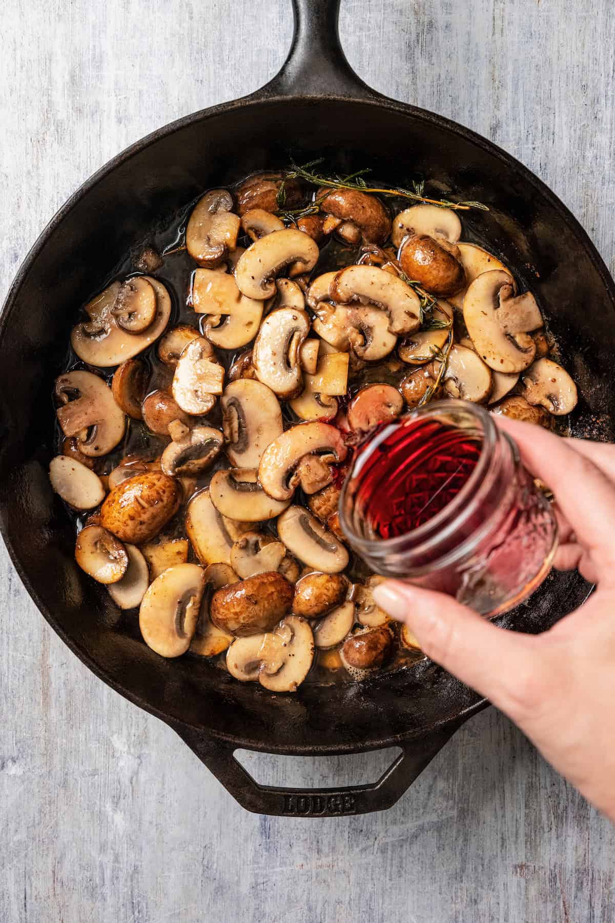 Adding wine to mushrooms cooking in a skillet.